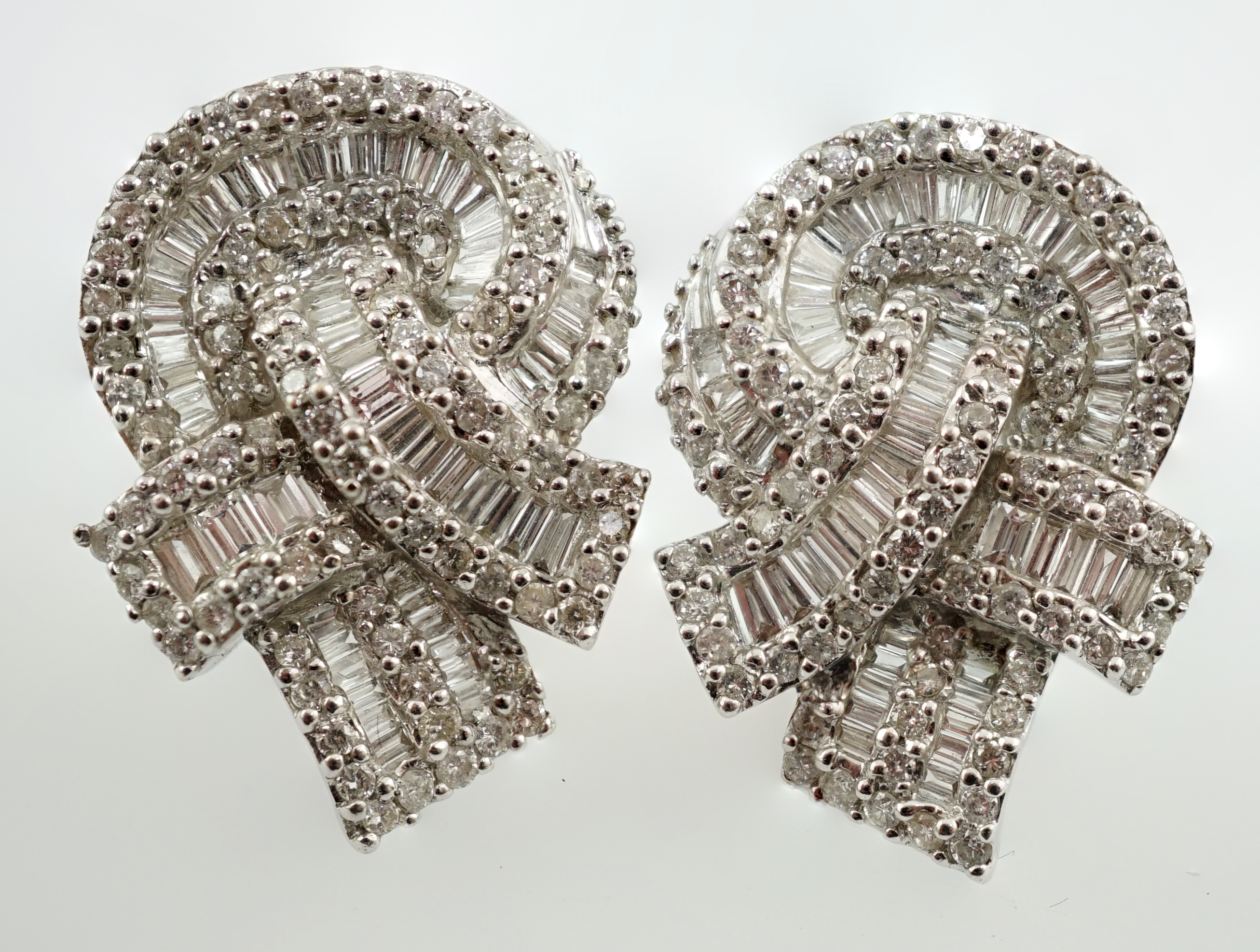 A pair of 18k white gold and pavé set round and baguette cut diamond cluster set 'knot' earrings